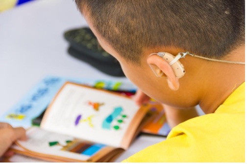 Child wearing a hearing aid, looking at a book.