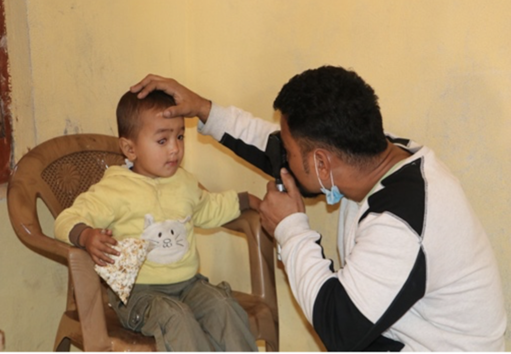 A person using a medical instrument to look into a toddlers eyes.