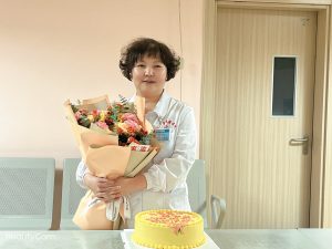 Author holding a bouquet of flowers standing in front of a cake.