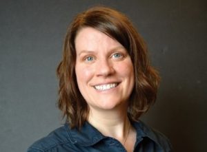 Photo of Kelli Hallsten Erickson, head and neck, woman with redd0sh shoulder length hair, smiling, wearing open neck blue.