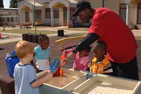 Teacher and four young children playing in the water table outdoors