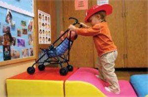 Toddler pushing a stroller up a soft ramp.