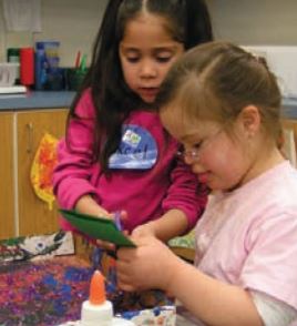 Two children, one with Down syndrome, cutting paper for an art project.