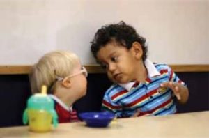 Two young boys sitting at a table. One boy is wearing glasses