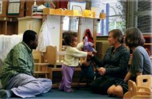 Parents, teacher and child sitting on the floor watching the child play